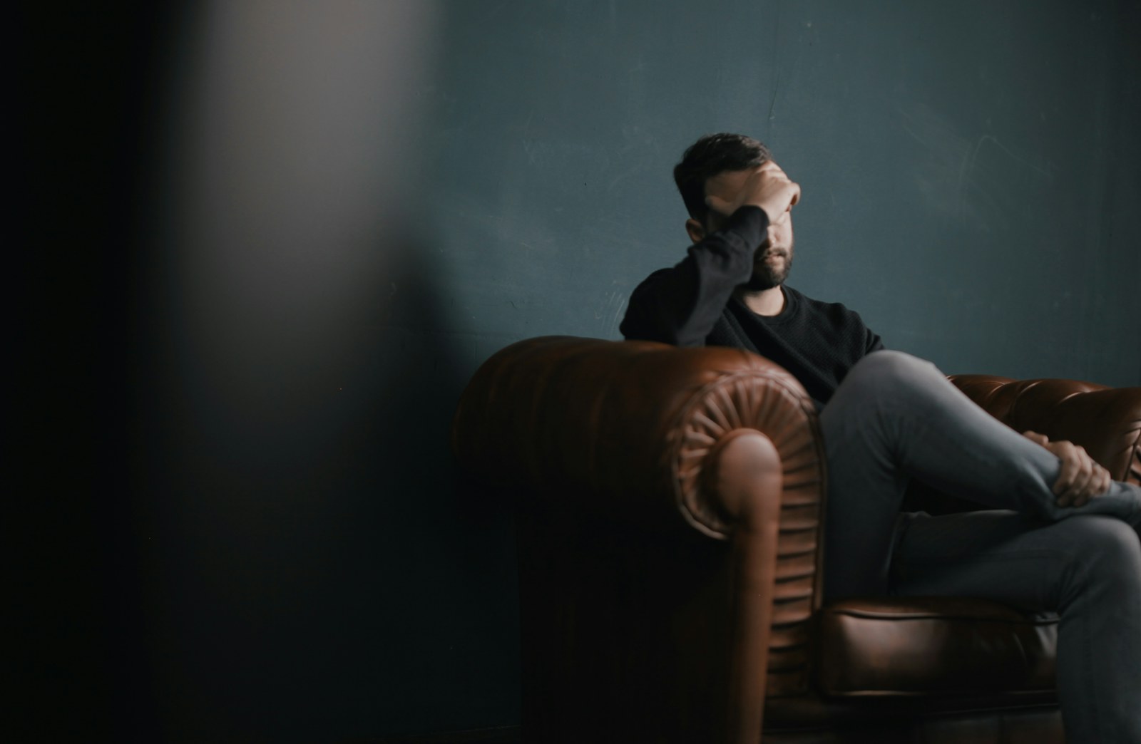 A person sitting quietly on a sofa with their hand resting near their forehead